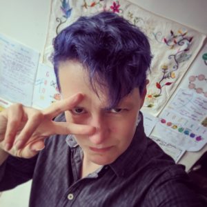 White non-binary person (me) with blue hair, looking determined